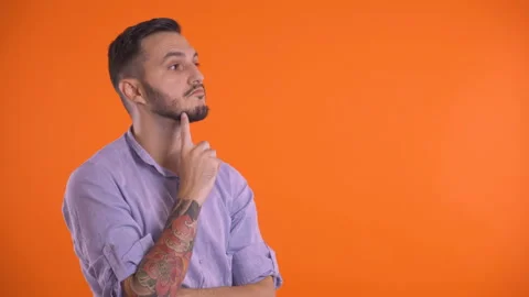 Thoughtful man looking up with finger on face or chin, isolated on orange Stock Footage 138925520