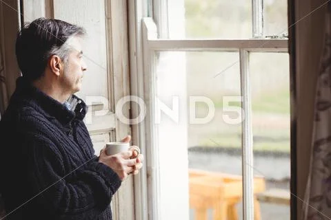 Thoughtful Man Looking Through A Window In His House