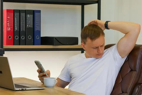 Thoughtful man scratching head while viewing phone in office Stock Photos