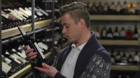 Thoughtful man selecting the perfect wine in a well-stocked supermarket Stock Footage 311235503