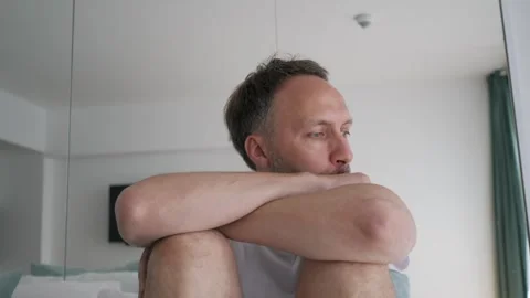 Thoughtful Man Sitting on Bed With Contemplative Expression in Bright Room Stock Footage 263365007