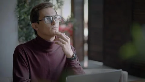 Thoughtful man is sitting at desk, working on laptop, thinking about solving Stock Footage 344800174