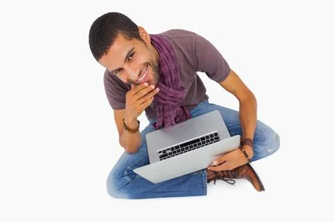 Thoughtful man sitting on floor using laptop and smiling at camera 스톡 사진