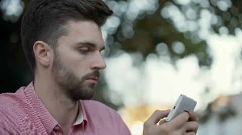 Thoughtful man sitting outdoor and texting on smartphone Stock Footage