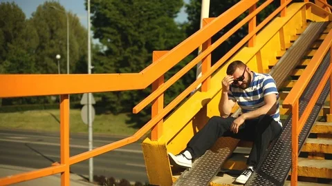 Thoughtful man sitting on the stairs next to the highway and looks really worrie Stock Footage