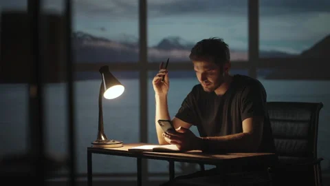 A thoughtful man sitting at a table with a desk lamp and a mobile phone. The Stock Footage 159766593