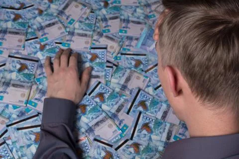 A thoughtful man is sitting at a table on which Kazakhstan's tenge money is l Stock Photos