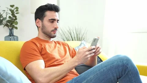 Thoughtful man with smartphone sitting on sofa Stock Footage 228949317