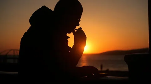 Thoughtful man smokes against the background of the sunset, writes in smartphone Stock Footage 150227630