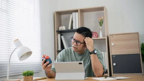 Thoughtful man solving stress by squeezing ball while working on digital ta.. 库存照片