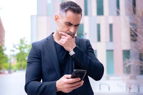 Thoughtful man in suit checking smartphone outdoors in urban setting Stock-Fotos