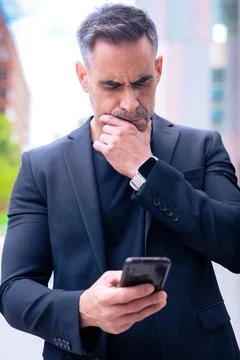 Thoughtful man in suit checking smartphone outdoors in urban setting.Vertical Stock-Fotos