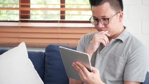 Thoughtful man using a digital tablet with a stylus on a couch Stock Footage 292606732