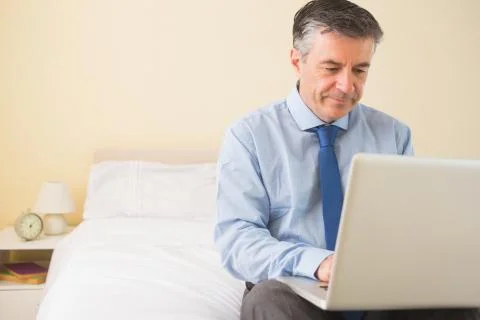Thoughtful man using a laptop sitting on a bed Stock Photos