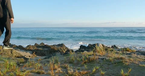 Thoughtful man walking on rocks beach at sunrise looking at ocean waves. 動画素材 220986778