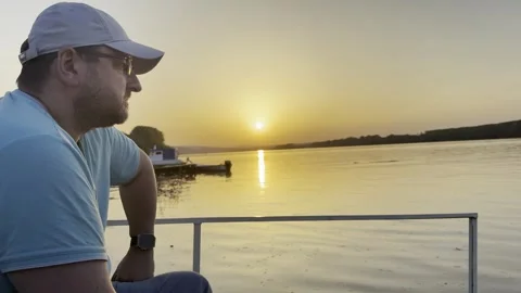 Thoughtful Man Watching Sunset Over Calm River 스톡 동영상 334570316
