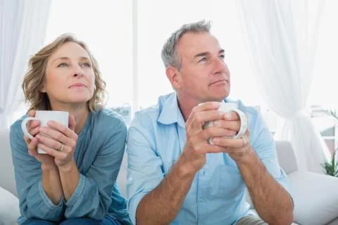 Thoughtful middle aged couple sitting on the couch having coffee Stock Photos