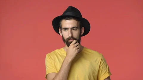 Thoughtful middle-eastern man in black hat, yellow t-shirt, rubbing beard as Stock Footage 115779076