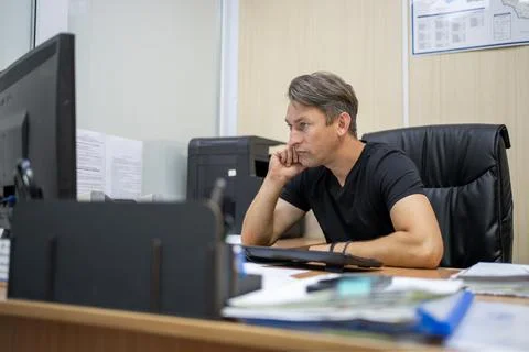 Thoughtful office worker resting his chin on his hand while looking at a co.. Stockfoto's