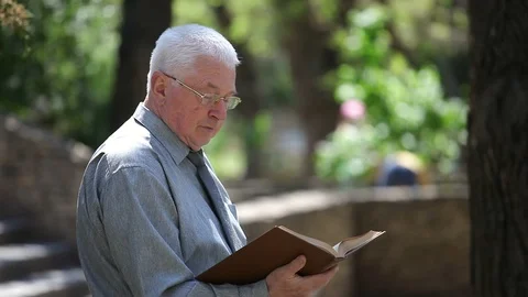 Thoughtful old man in glasses sits and reads in a street in summer Video stock 89948558