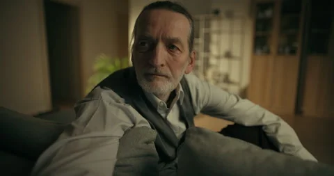 Thoughtful older man sitting on a sofa in a softly lit living room Stock Footage 336282738