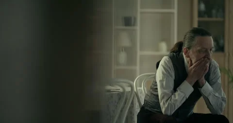 Thoughtful older man sitting by a window indoors Видео 336286243