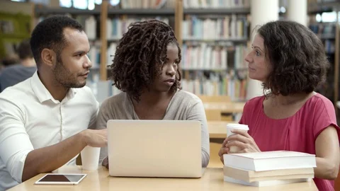 Thoughtful people talking while using laptop at library Stock Footage 117311981