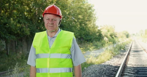 Thoughtful railroader in uniform looking at camera and crossing hands at track Stock Footage 135569940