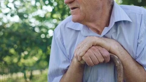 Thoughtful sad senior looks at camera and tilts head on hands in garden. 4K Video stock 80946532