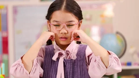 Thoughtful Schoolgirl Adjusting Glasses While Concentrating in Classroom Stock Footage 324929874