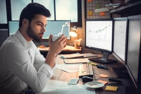 Thoughtful serious trader broker drinking coffee analyzing stock market graphs Stock Photos