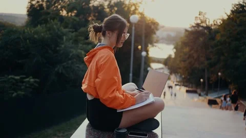 Thoughtful student doing homework in the park, thoughtfully writing notes, with Video stock 160484615