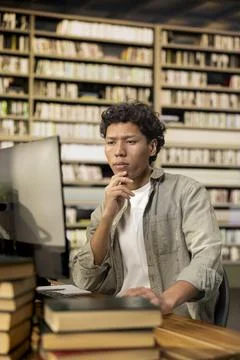 Thoughtful student sitting at computer desktop in wooden library table Stockfoto's