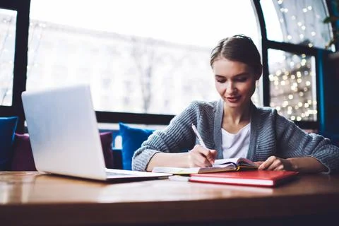 Thoughtful student taking notes in notebook while working on project in cafe Stock Photos