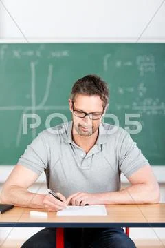 Thoughtful teacher checking examination papers at bench Stock Photos