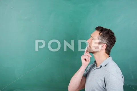 Thoughtful teacher with hand on chin against blackboard Stock Photos