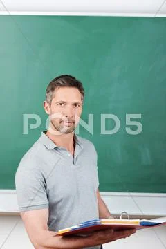 Thoughtful teacher holding binder against blackboard Stock Photos