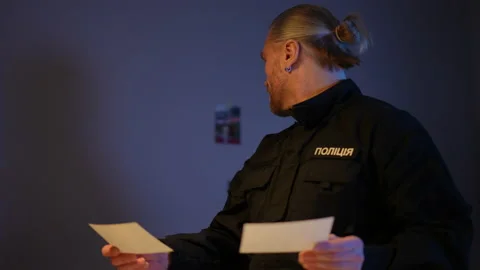 Thoughtful Ukrainian cop comparing new crime photos and pictures hanging on the Vídeos de archivo 173549534