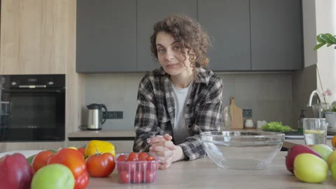 Thoughtful Woman Looking At Camera While Standing In Kitchen With Vegetables Stock Footage 308454878