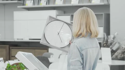 Thoughtful woman selecting between two stylish wall clocks in a chic furnishings Stock Footage 311544868