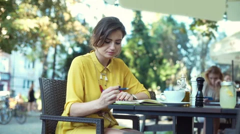 Thoughtful woman sitting in the outdoor cafe and reading her journal Stock Footage