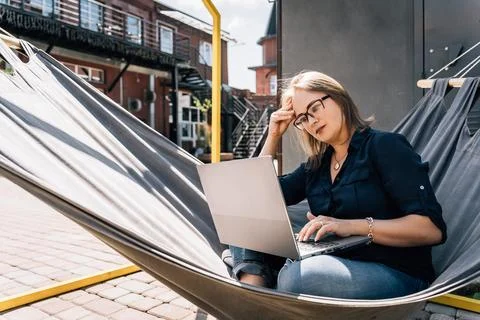 Thoughtful woman solving complex problem on laptop in urban hammock Stock Photos