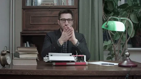 Thoughtful writer sitting in front of typewriter waiting for inspiration for his Vídeos de archivo 73685118