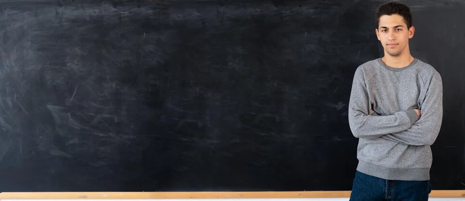 Thoughtful young arabic man standing next to empty chalk board at school or u Stock Photos