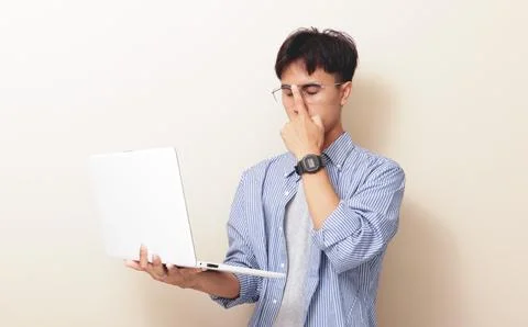 Thoughtful young Asian IT man using laptop and holding chin with thinking g.. Stock Photos