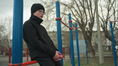 Thoughtful Young Boy Sitting on Red Bar in a Quiet Outdoor Park 스톡 동영상 283169604