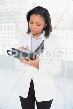 Thoughtful young dark haired businesswoman taking notes on her schedule Stock Photos