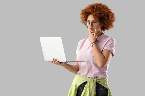 Thoughtful young female programmer with laptop on grey background Stock Photos