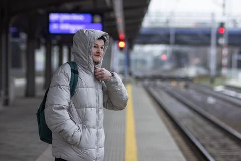 Thoughtful young man in casual gray jacket and hat with backpack standing and Stock Photos