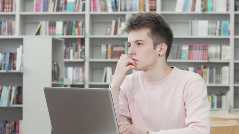 Thoughtful young man engaged in online work at a library Stock Footage 311991953